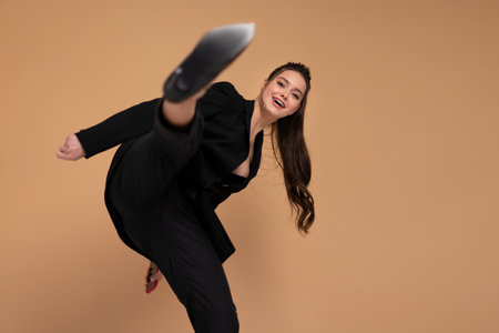 Businesswoman hitting with leg in camera dressed black office suit smile isolated on color background. Fight for businessの写真素材