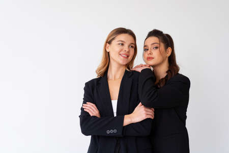Concept of partnership in business. Two Young businesswoman dressed black formal suit standing studio isolated white background. Brunette woman put her hands on the shoulders of her friend.の写真素材