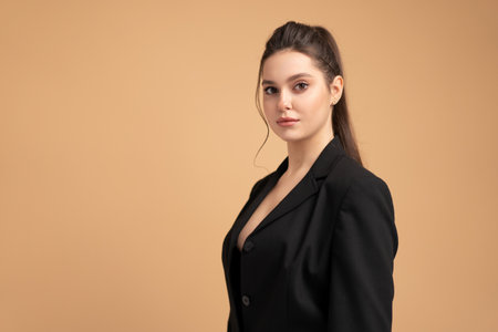 Young business woman close up portrait dressed black jacket standing studio isolated on color background. Caucasian female business person looking at camera with serious face. Medium shoot side viewの写真素材