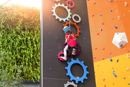 Child climbing on wall in amusement centre. Climbing training for children. Little girl in dressed climbing gear climb high. Extreme active leisure for kids. Caucasian little girl 5 years old.の写真素材