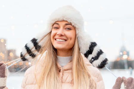 Medium shoot portrait of romantic european lady wears stylish winter jacket and funny fluffy hat in snowy day. Outdoor photo of inspired blonde woman enjoying free time in winter city. Christmasの写真素材