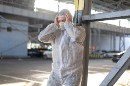 Despair healthcare worker in white covid protective overalls.Tired Male caucasian doctor grabs his...