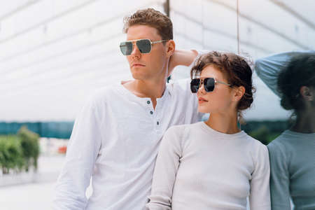 Smiling beautiful woman and her handsome boyfriend. Woman in casual summer jeans. Serious pensive couple in sunglasses walking business district. Couple posing on the street modern building backgroundの写真素材
