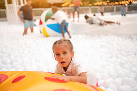 Happy little girl playing white plastic balls pool in amusement park. playground for kids. Active leisure for children.の写真素材