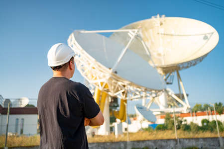 Engineer looking earth based astronomical radio telescope. Radio telescopes used in science for space observation and distant objects exploring. Caucasian man white protective helmet satellite dishesの写真素材