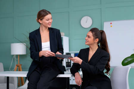 Young women leaders are checking financial statements from paper documents. Two female confident business worker dressed black suit in office checking financial document looking folder and discussingの写真素材