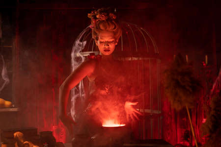 Halloween witch with cauldron. Beautiful young woman conjuring, making witchcraft. Standing spooky...
