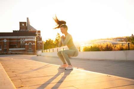 Sporty woman doing jumping squats exercises on stairs in park. Bodyweight training on sunset. Young...