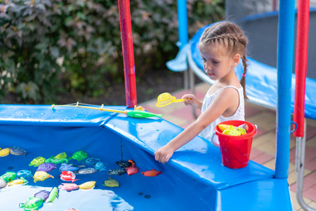 Child Fisher Catching Plastic Toy Fish On Pool Amusement Park Summer Day Little Girl Have Fun On Fishing Carnival Festival Entertainment For Childrenの写真素材