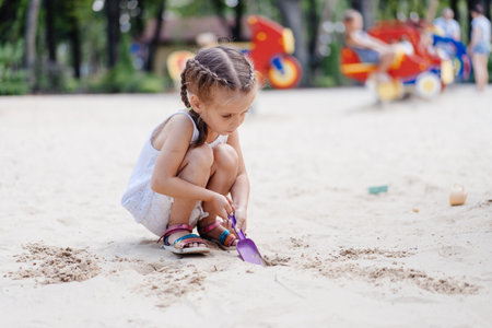 Little Girl Playing Sandbox Playground Digging Sand Shovel Building Sand Figure Summer Day. Caucasian Female Child 5 years Have Fun Outdoorの写真素材