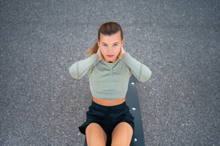 Sit-up exercises. Active, fit sporty woman doing situps, exercising and training on fitness outdoor gym. One young, serious and athletic female exercising, high angle viewの写真素材