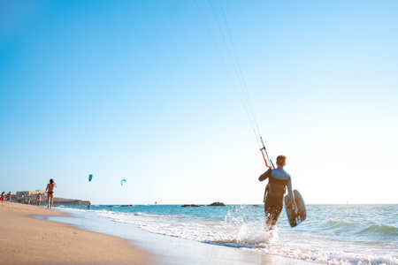 Portrait wave kitesurfer walking upwind at the beach with his board and kite. Man kite surfer walk sand ocean beach with his kite surf board.の写真素材