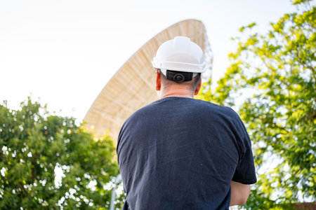 Engineer looking earth based astronomical radio telescope. Radio telescopes used in science for space observation and distant objects exploring. Caucasian man white protective helmet satellite dishesの写真素材