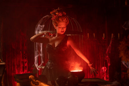 Witch with cauldron. Beautiful young woman conjuring, making witchcraft. Standing spooky dungeon dark room. Enchantress prepare love potion use magic spellの写真素材
