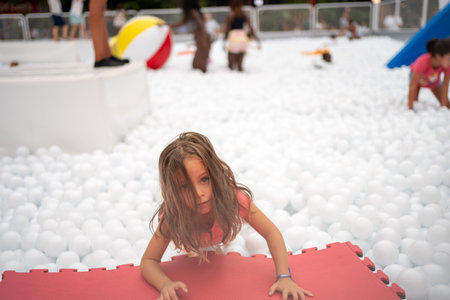 Happy little girl playing white plastic balls pool in amusement park. playground for kids. Active leisure for children.の写真素材