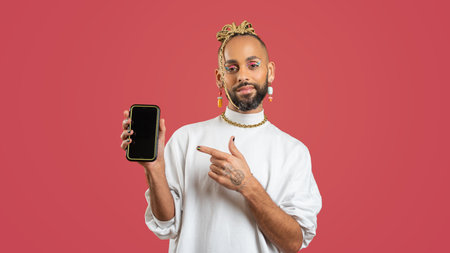 Young smiling african-american gay man wear sweatshirt hold in one hand mobile phone pointing on...