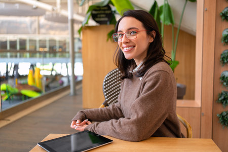 Woman student with tablet computer sitting at her desk smile and looking away. Female person studying or working online on touch pad. Modern technologies and communication.の写真素材