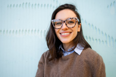 Happy woman in glasses outdoor on blue color background. positive people concept. Smiling girl in eyeglasses looking at cameraの写真素材