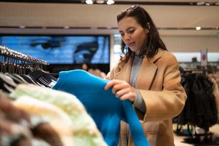 Woman dressed in stylish trench coat walks shopping mall chooses sweater in clothing storeの写真素材