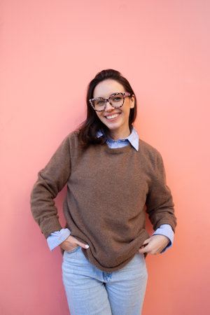 Happy woman in glasses outdoor on yellow and pink color background. positive people concept. Smiling girl looking at camera, hands in pocket, dressed sweater and jeansの写真素材