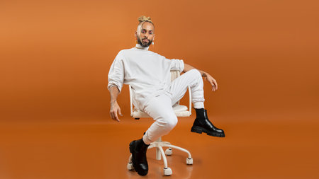 Trendy black latin gay man in white clothes sitting chair look camera isolated on orange background studio portrait People lifestyle fashion lgbtq conceptの写真素材