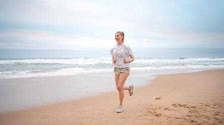 Woman jogging on beach. Sporty female jogging on sand beach, waves on background. Full body view...