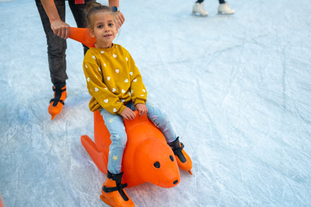 Child glides across ice rink on toy. Child glides across ice rink. Family socializing in winter, playing sports and having fun in snow. Daughter enjoying winter activitiesの写真素材