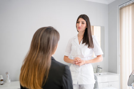 Female professional beauty doctor talking with young female. Beauty therapist talks to client about facials procedure. Dermatologist and patient in clinicの写真素材