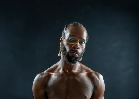 Confident african-american bearded gay man with bright makeup isolated on black, Close up portrait gay African muscular shirtless man wearing make-up looking at camera.の写真素材