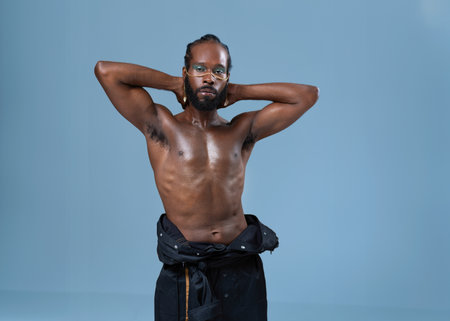 Confident shirtless african-american gay with bright makeup isolated on blue background, Gay African...
