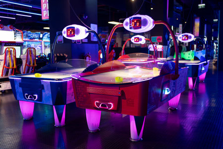 Air hockey tables illuminated neon light childrens entertainment center, accompanied by various gaming machines in an arcade.の写真素材
