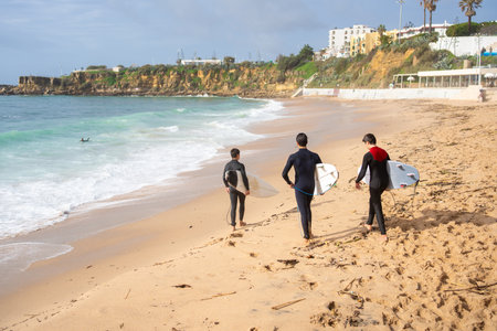 Back view of anonymous surfers walking with surfboards along sea waves. Full body of active friends in swimwear walking on sandy beach. Summer vacation and water sport concepts.の写真素材