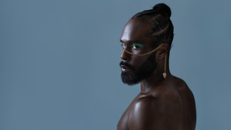 Side view of bearded African American gay man with light makeup and gold accessory on face. Senior...