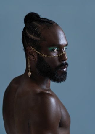 Portrait of serious African American shirtless gay man with bright makeup and gold accessory on...