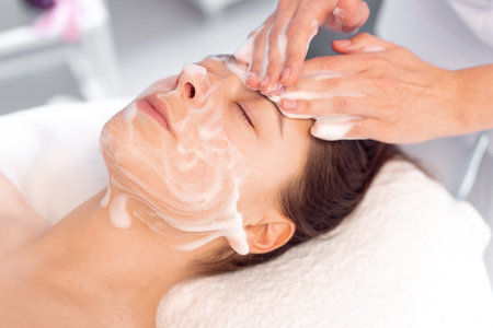 Cosmetologist cleanses the skin with foam. Womans skin care procedure in beauty clinic. Natural cosmetics. Cosmetic treatment of face. Therapeutic peeling cream.の写真素材