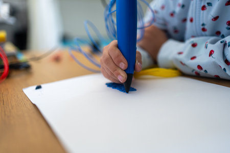 3D pen Close-up of girl creating plastic 3D model, drawing. Unknown childs hand draws with pen on...
