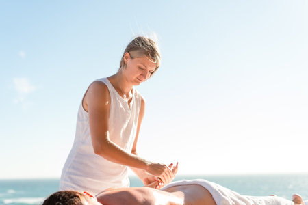 Female manual therapist massaging female arms outdoor. Professional masseur female giving spa massage client lying on special table, blue sky in background. Healthy lifestyle and body careの写真素材