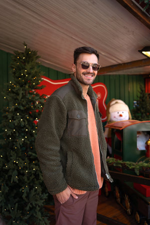 Festive location: Good looking man in green jacket enjoying Christmas city decorations. Elegant male wearing sunglasses watching Christmas city.の写真素材