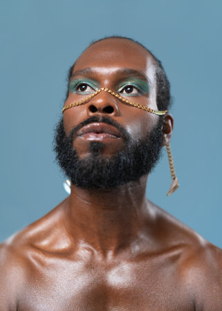 Thoughtful African American bearded gay man with bright makeup on blue background, Close-up portrait. Exudes sense of pride and individuality. Diversity power of personal style.の写真素材