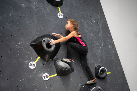 Courageous girl climbing artificial rock wall at bouldering gym. Low angle side view of sporty female child is training on equipment.の写真素材