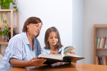 Grandmother and granddaughter reading book together at home. Cute girl turning pages as elderly woman sits with her, children education conceptの写真素材