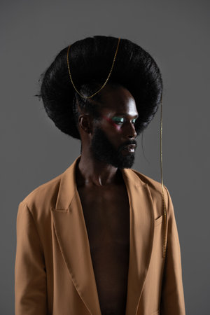 Serious African American model wearing huge wig with chain over black background. Black man is wearing blazer in studio.の写真素材