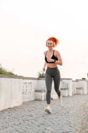 Sporty jogger female running on footpath against clear sky. Full body of young woman in activewear listening music while exercising during daytime.の写真素材