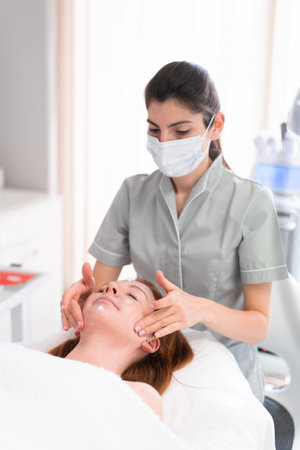 Cosmetologist massaging womans face at beauty salon. Relaxed female customer is getting pampered in spa by beautician.の写真素材