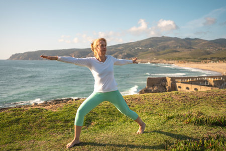 Senior woman doing yoga performing asanas on ocean shore. Active retired female taking care her body and enjoying life in sunny morning. Retirement, relaxation, vacation, healthy senior lifestyleの写真素材