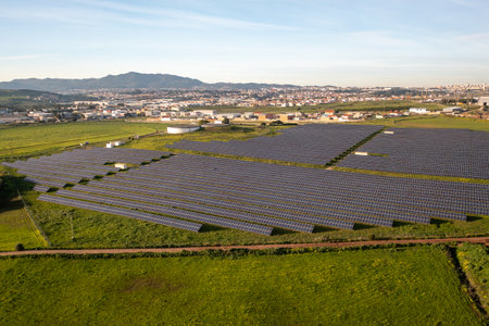 High angle drone view of solar panels on agricultural field during daytime. The vast landscape is...