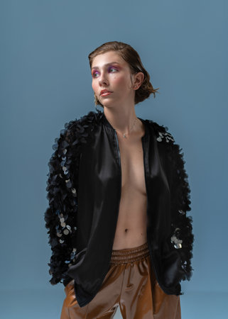 Thoughtful sensuous female model with hands in pockets wearing black jacket on blue background. Woman is standing while posing in studio.の写真素材