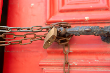 Closeup of metallic chains and locks in handles on red closed vintage doors. Full frame shot of vibrant wooden entrance outdoors.の写真素材