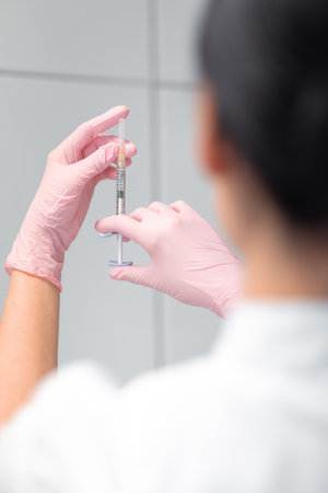 Anonymous female cosmetologist holding injection syringe in clinic. Back view of unrecognizable skin therapist in beauty spa salon.の写真素材