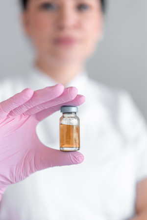 Anonymous female cosmetologist holding medicine bottle for injection in clinic. Professional skin therapist is wearing pink glove beauty spa salonの写真素材